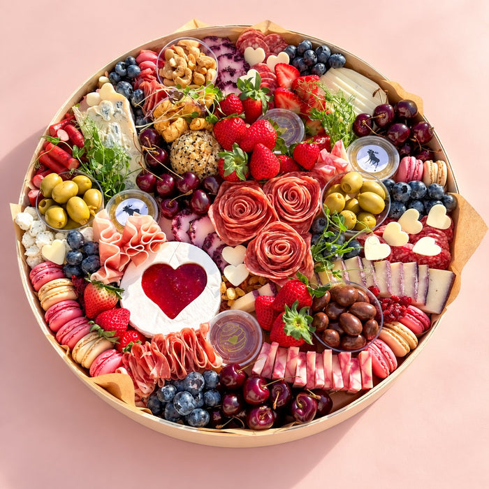 Overhead charcuterie board with many types of cheese, a heart shaped brie, salami roses and cherries