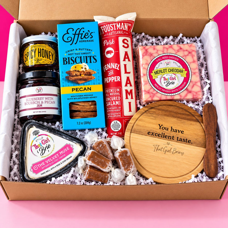 The Excellent Taste Box, a gourmet cheese gift box and cheese board gift set, on a hot pink background