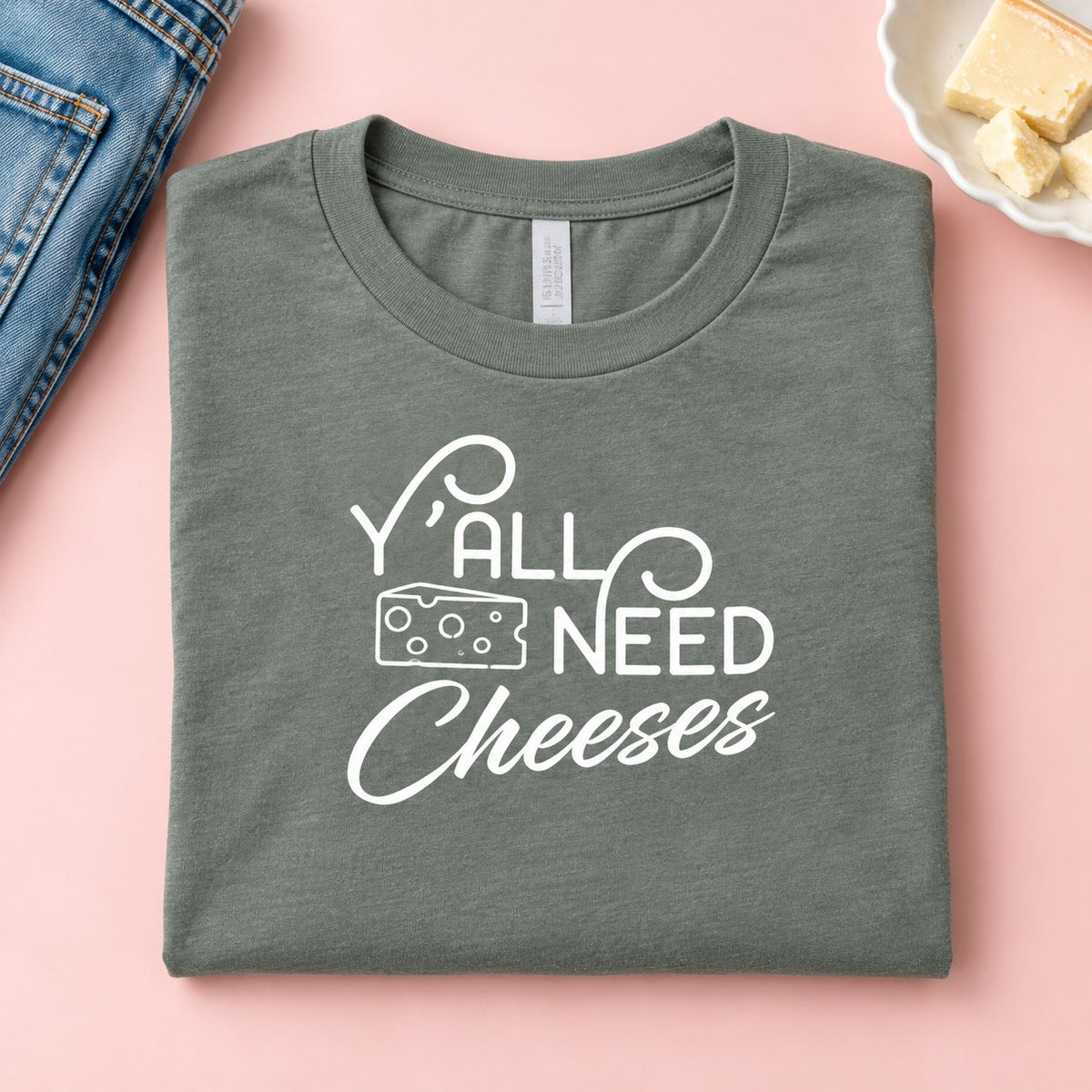 Folded heather green Y'all Need Cheeses t-shirt with cheese and jeans