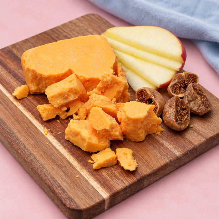 Crumbly aged cheddar on a wooden cheese board with sliced apple and dried figs