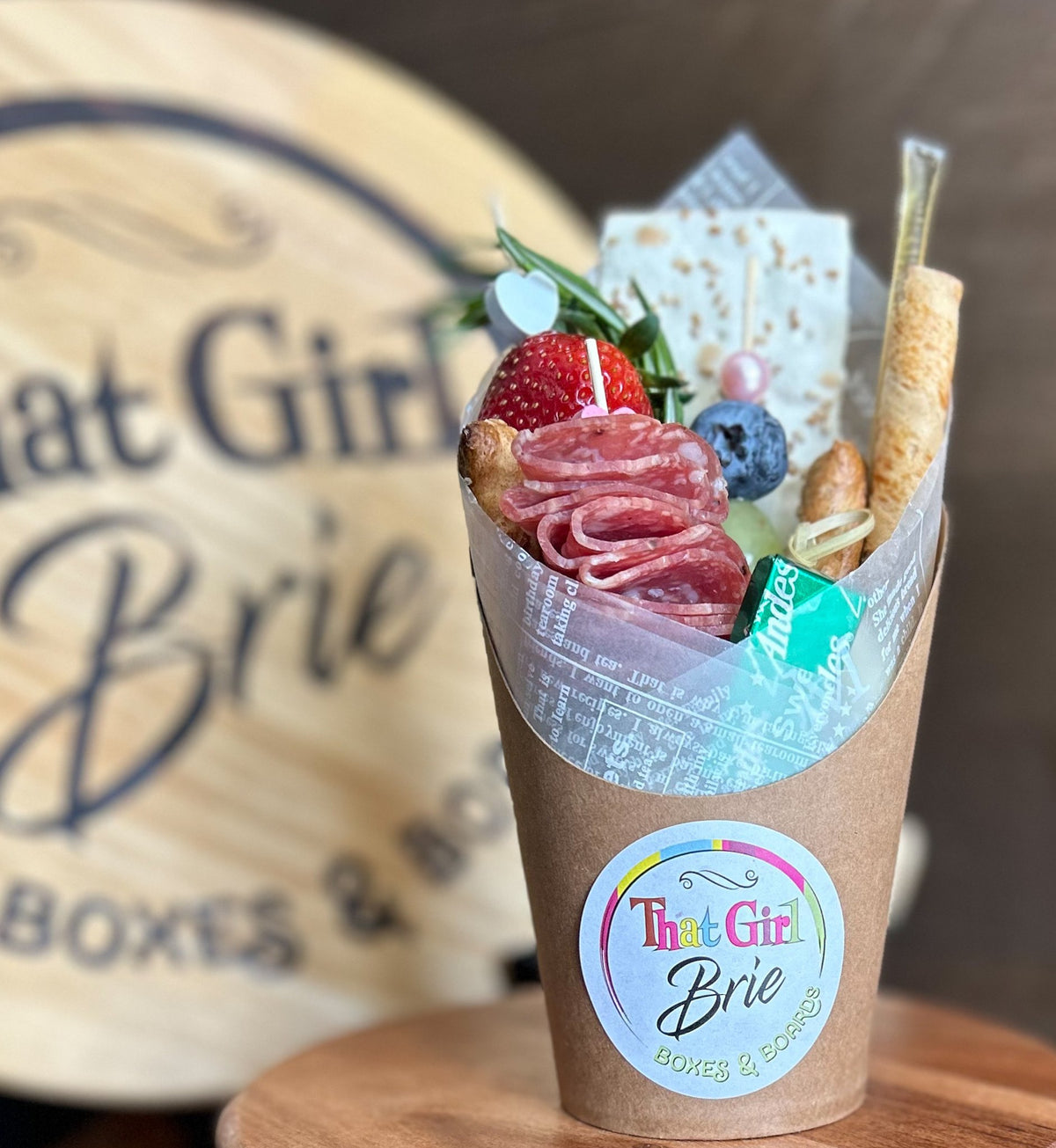 Individual charcuterie cup with salami, strawberry, blueberry, cheese, breadsticks and a That Girl Brie sticker