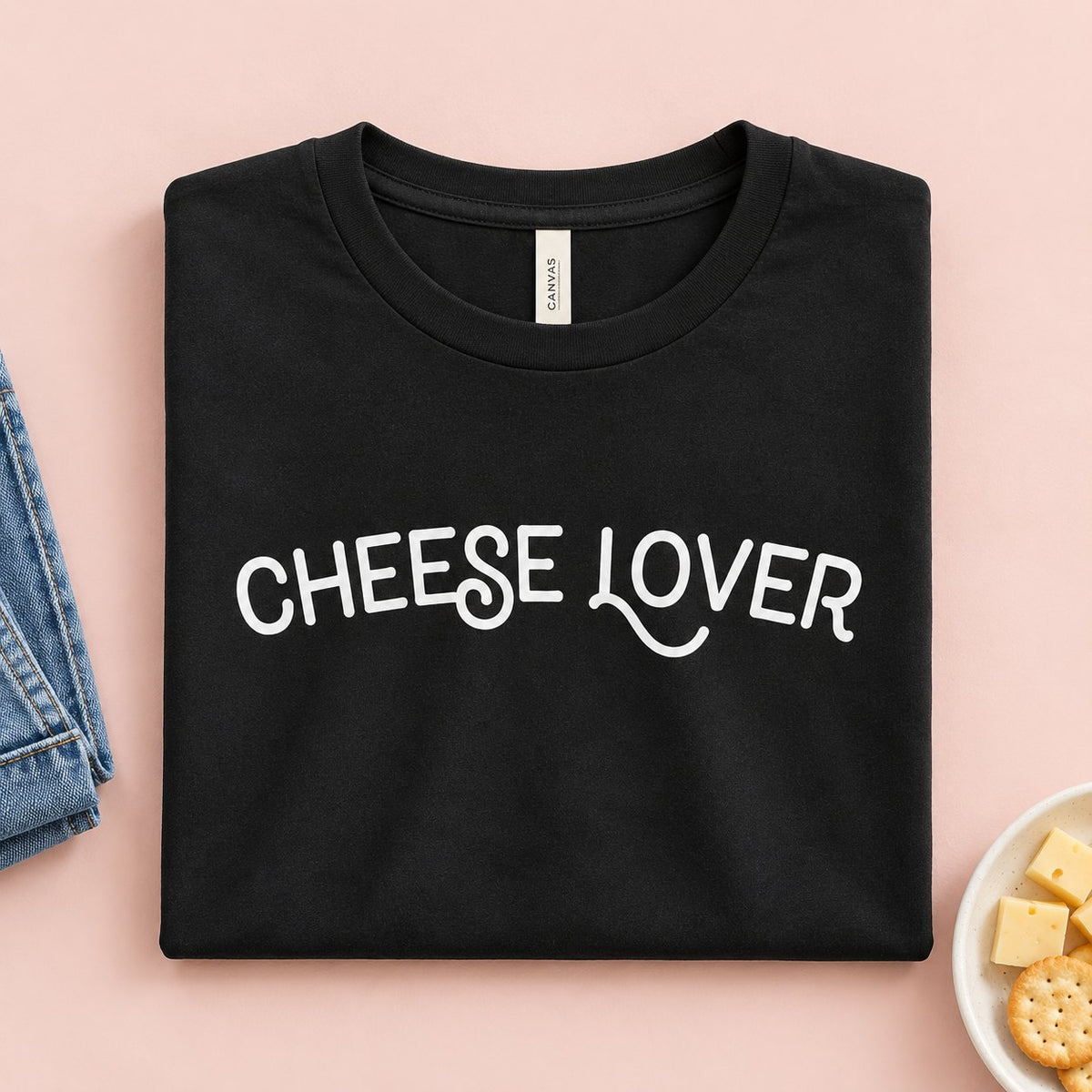 Cheese Lover t-shirt folded flat with jeans, cheese cubes and crackers
