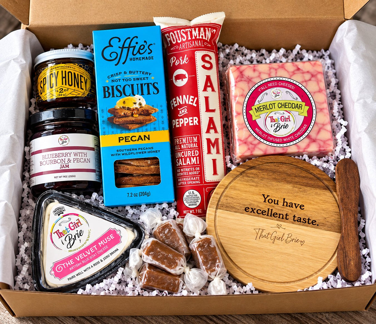 The Excellent Taste Box gourmet cheese gift box open on a wood table with a mini serving board and spreader