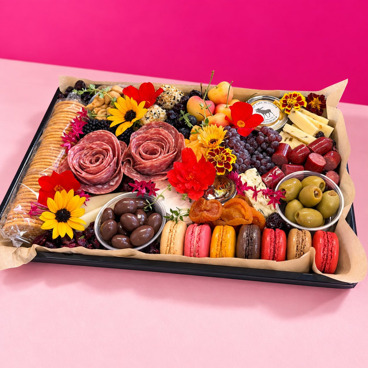 The Gather Board charcuterie platter with cured meats, macarons and dried apricots in front of a pink wall