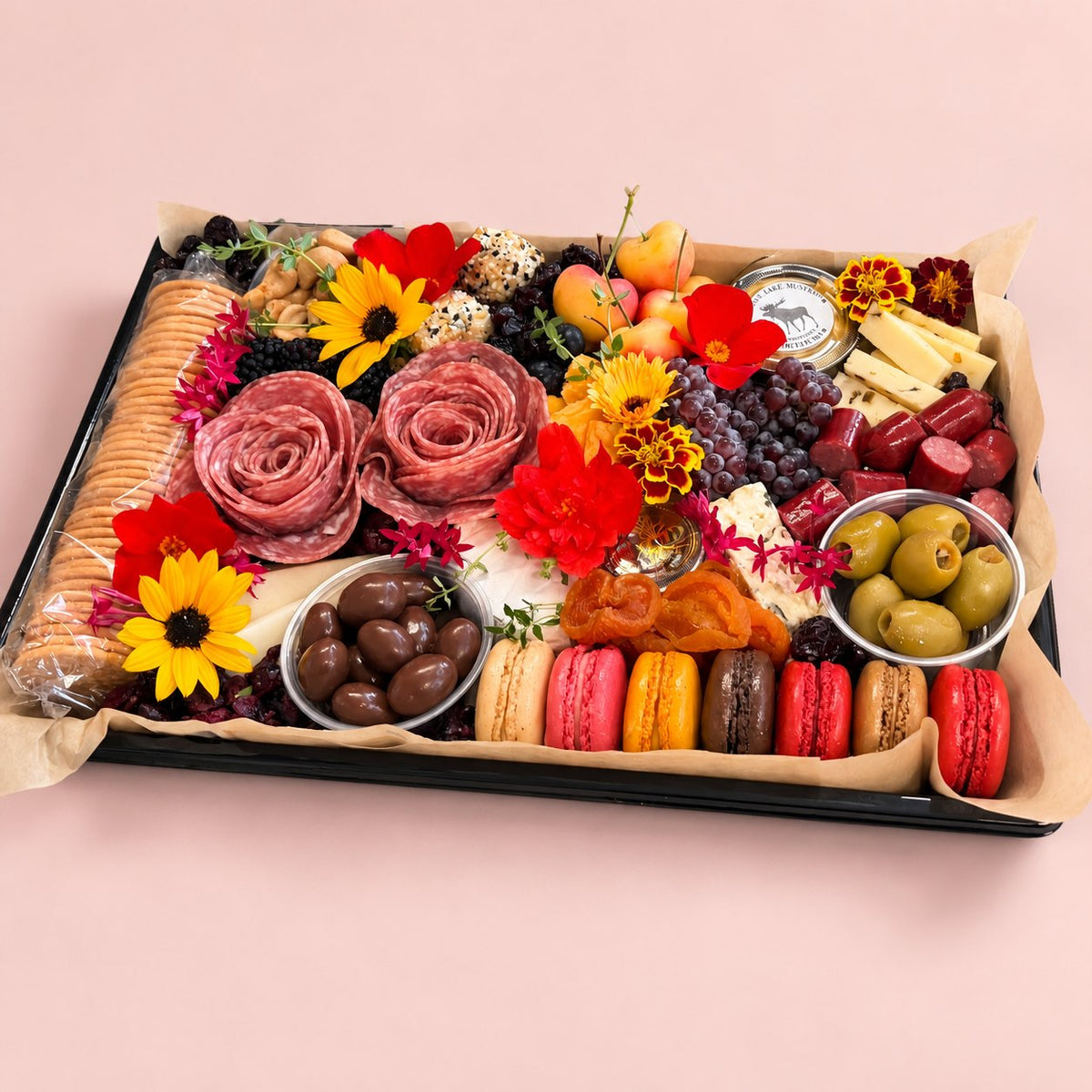 The Gather Board charcuterie platter with salami roses, macarons, cheeses and edible flowers on a pink background