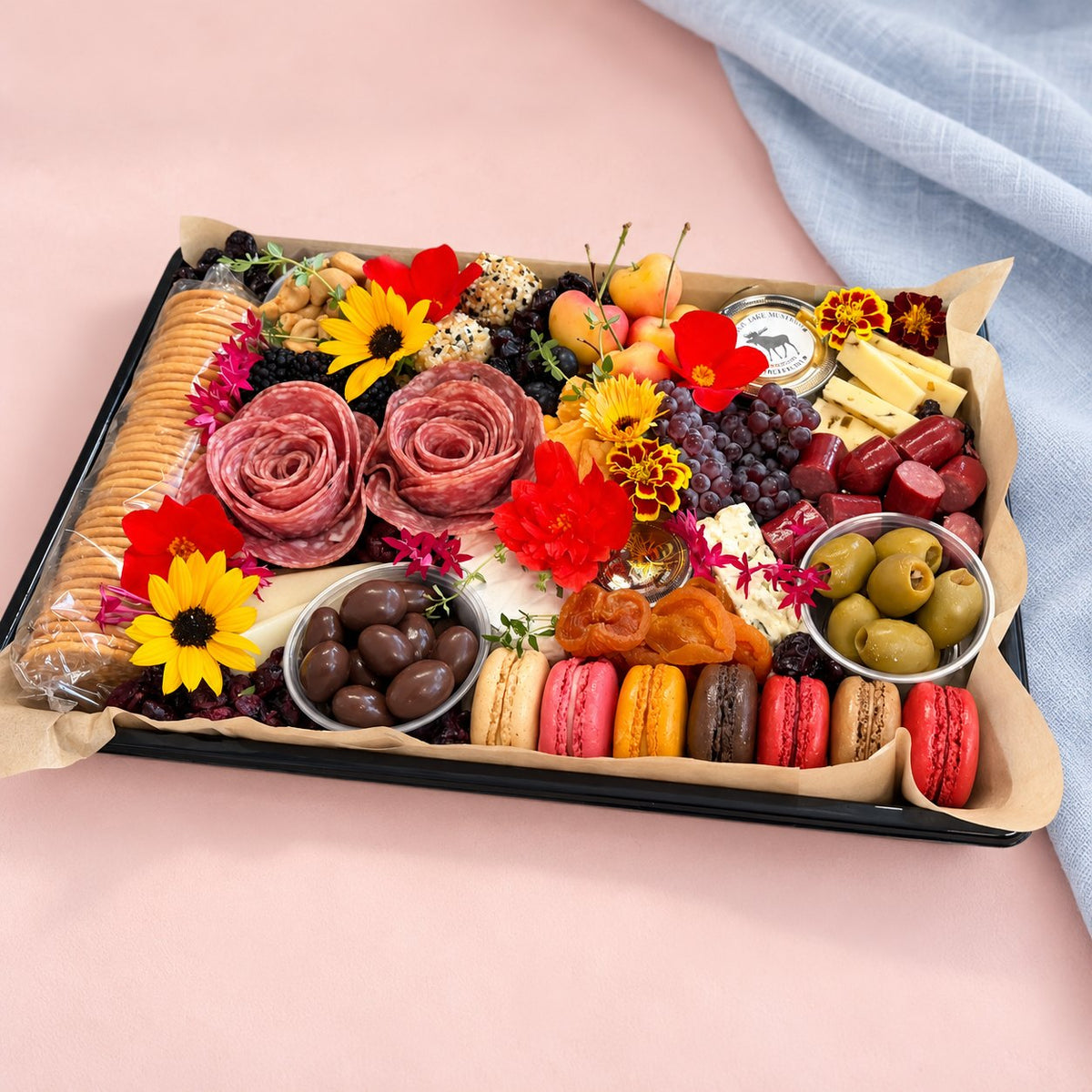 The Gather Board charcuterie platter with Wisconsin cheeses, olives, fresh fruit and flowers beside a blue linen