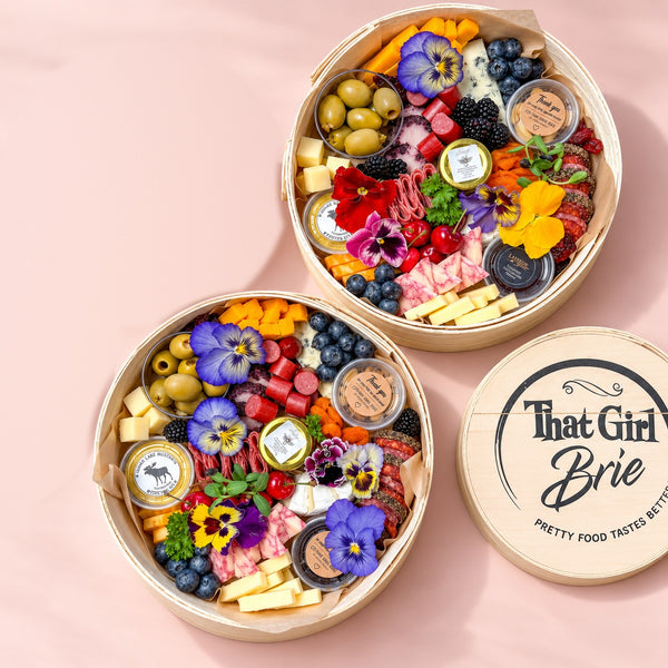 The Keepsake premium charcuterie board in two sizes, Signature and Grand Gift, with a That Girl Brie keepsake lid