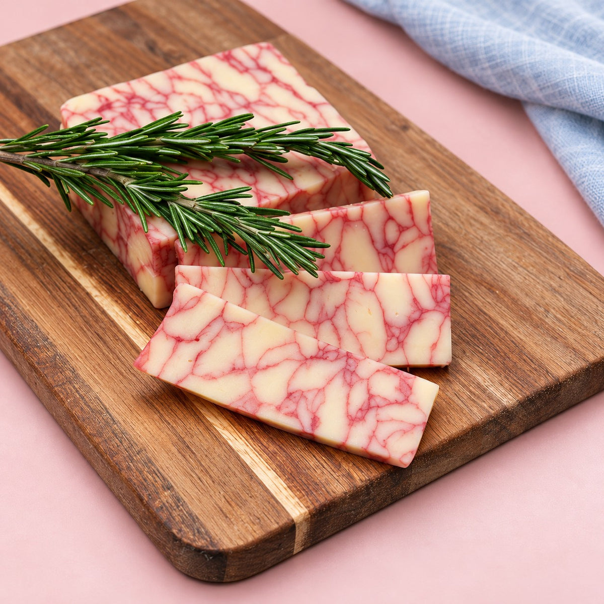 Sliced Merlot Cheddar wine cheese with rosemary on a cheese board with a blue linen napkin