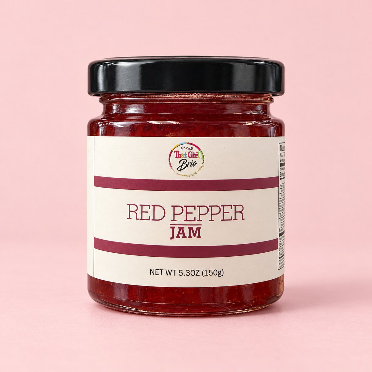 Jar of That Girl Brie Red Pepper Jelly, a sweet pepper jelly, on a light pink background